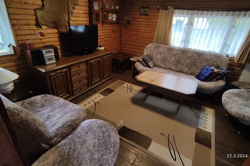 Wohnzimmer mit bequemer Couch, Tisch, TV und Lampe.