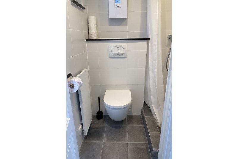 Stilvolles Badezimmer mit moderner Toilette, Fliesen und Holzboden.