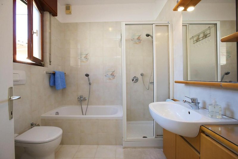 Freundliches Badezimmer mit Dusche, kleiner Badewanne, Bidet und Fenster