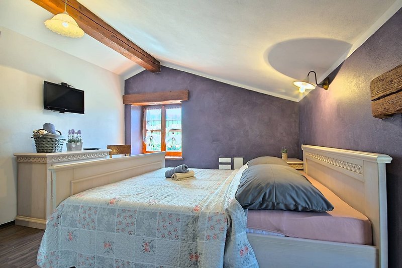 Schlafzimmer mit Holzbett, Bettwäsche und gemütlicher Beleuchtung.