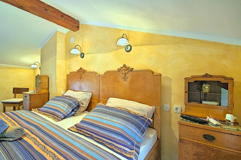 Schlafzimmer mit Holzbett, Bettwäsche, Kissen und Lampe.