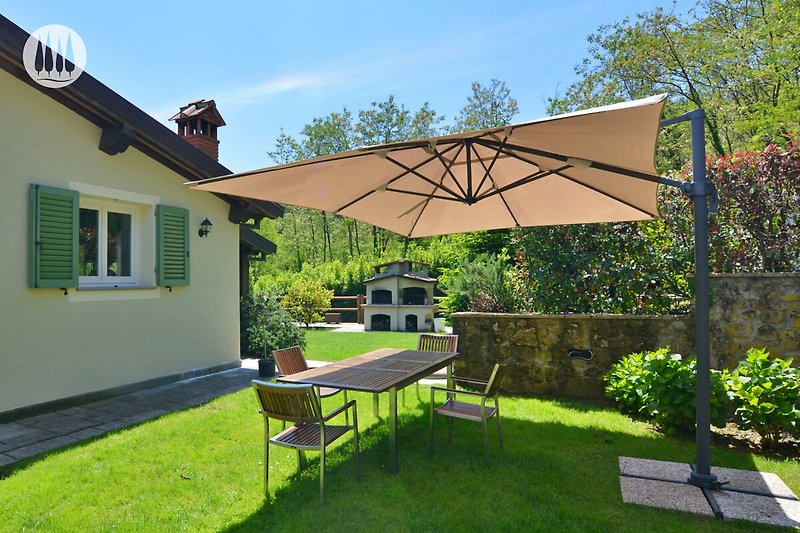 Haus mit Garten, Tisch, Stühlen, Sonnenschirm und Pflanzen.