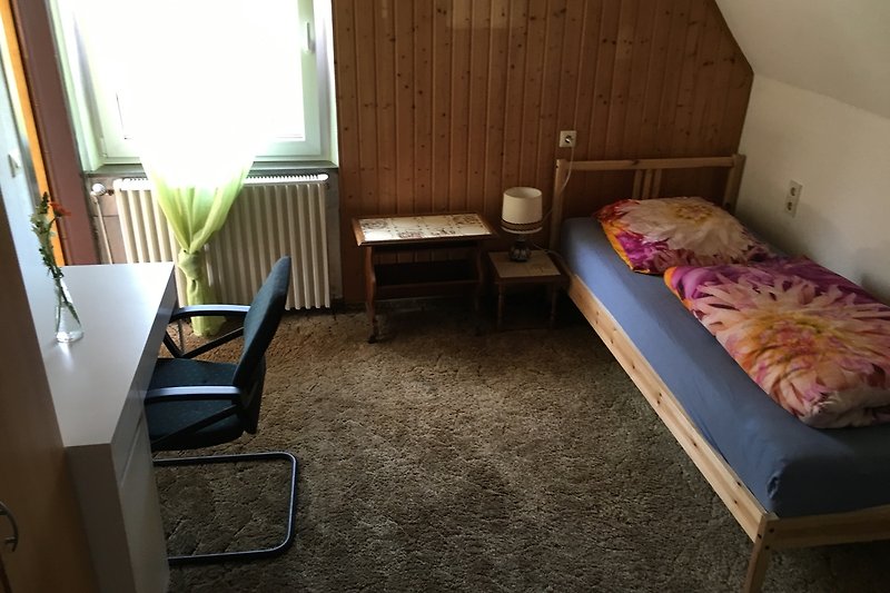 Schlafzimmer mit Bett, Kissen, Fenster und Pflanze.
