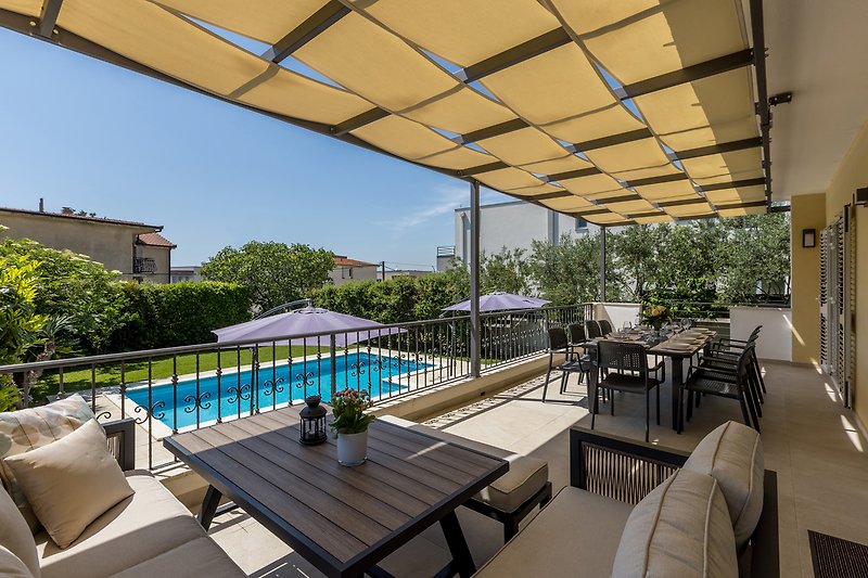 Relax by the poolside in this stunning outdoor setting with comfortable furniture and lush greenery.