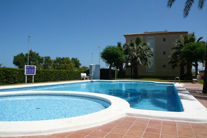 Luxuriöses Apartment mit Pool und Palmen, umgeben von grüner Landschaft.