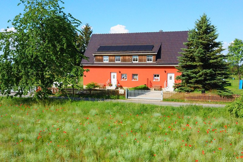 Ländliches Haus mit blühendem Garten und grüner Landschaft.