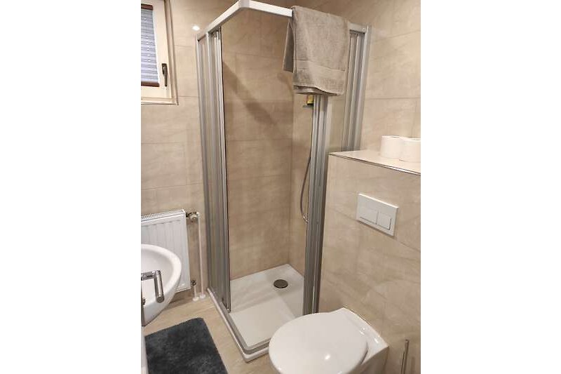 Gemütliches Badezimmer mit lila Duschkopf, Toilette und Duschabtrennung.