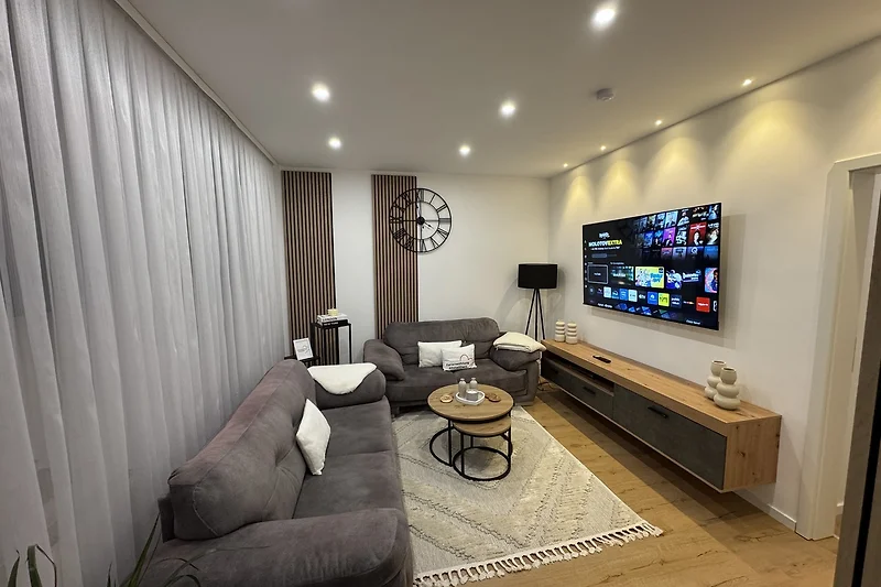 Wohnzimmer mit grauem Sofa, LCD-TV, Couchtisch und Bücherregal.