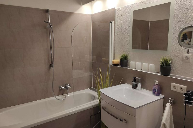 Badezimmer mit Spiegel, Waschbecken, Badewanne und Dusche.