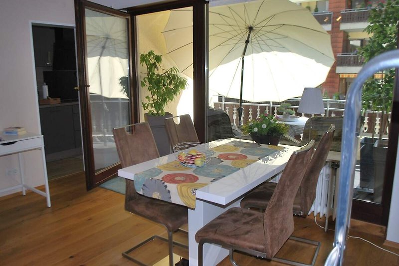 Schattiger Außenbereich mit Tisch, Stühlen und Sonnenschirm.