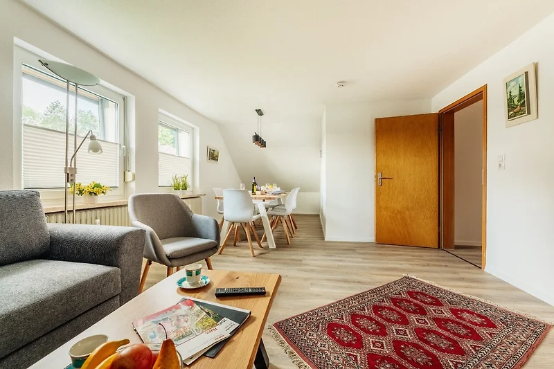 Wohnzimmer mit Couch, Sessel, Holztisch, Pflanzen und Lampe.