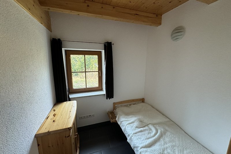Schlafzimmer mit gemütlichem Bett, Holzdecke, Fenster.