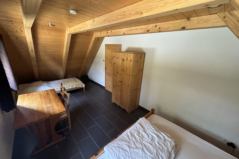 Holzdecke, Dachbalken, gemütliches Bett, Holzleiter, rustikales Zimmer.