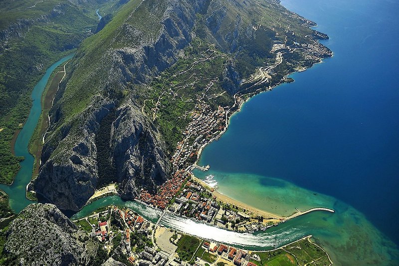 In Omiš, an emerald green river flows into the blue sea, surrounded by steep cliffs.