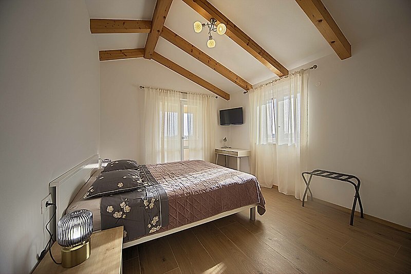 Schlafzimmer mit Holzbalken, Bett und Fensterblick.