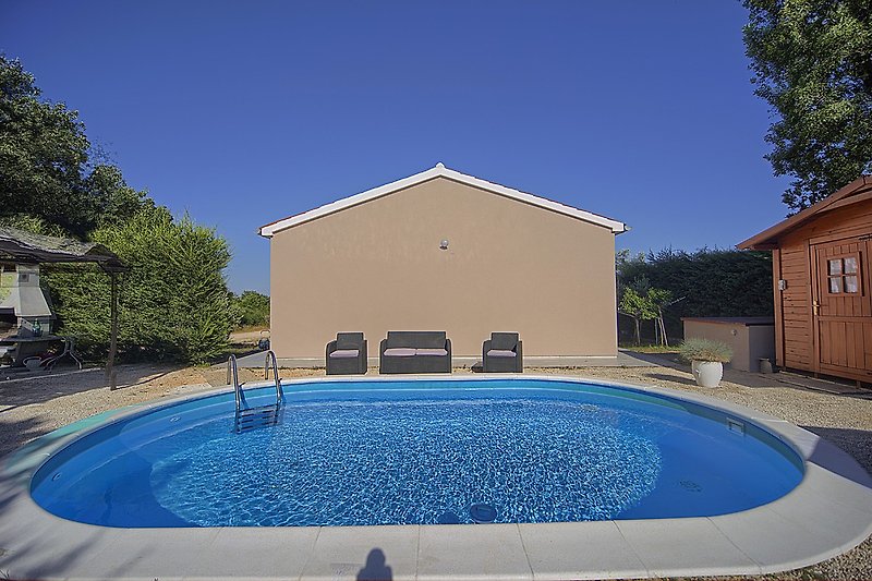 Schwimmbad mit azurblauem Wasser, umgeben von Pflanzen und Schatten.