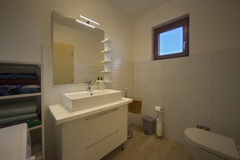 Moderan interijer kupaonice s drvenim ormarićem, ogledalom i slavinom.