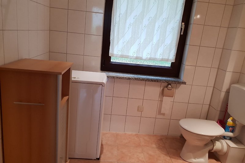 Badezimmer mit Waschmaschine, Fenster und Toilette.
