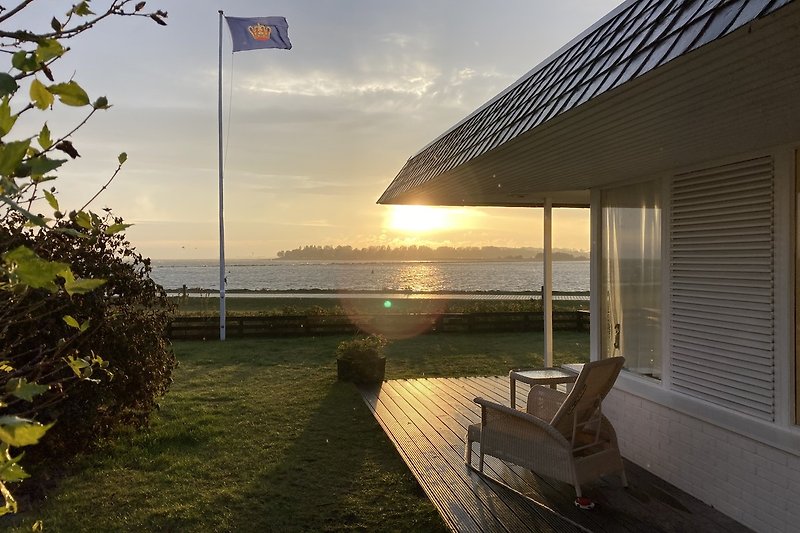 Holzhaus am See mit Terrasse, Sonnenuntergang und üppiger Natur.