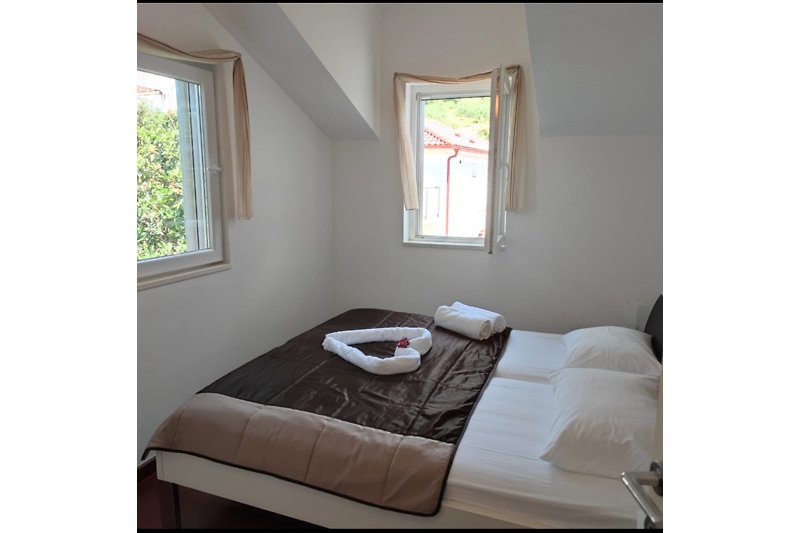 Schlafzimmer mit gemütlichem Bett, Fenster und Holzboden.