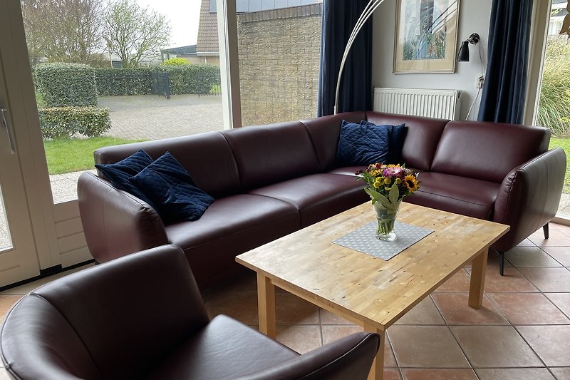 Modernes Wohnzimmer mit bequemer Couch, Tisch, Pflanze und großem Fenster. Gemütliche Atmosphäre.