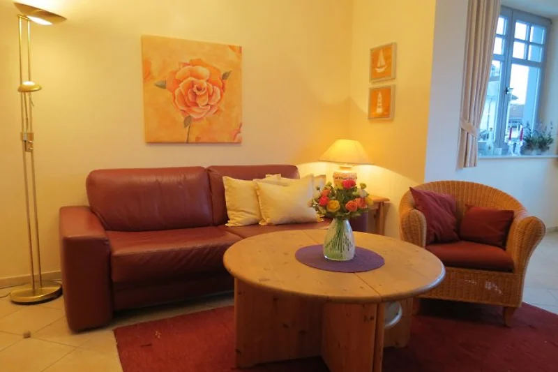 Gezellige woonkamer met een grote, comfortabele bank gericht op een moderne televisie. De kamer is sfeervol ingericht met warme kleuren en zachte verlichting. Er zijn kussens en dekens op de bank voor extra comfort, en aan de muur hangen kunstwerken die d