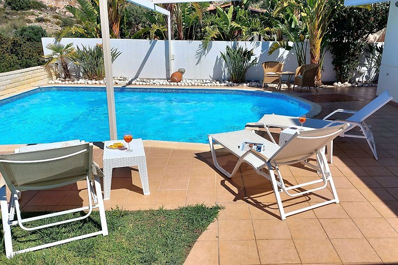 Piękny dom wakacyjny z basenem i meblami na zewnątrz, otoczony tropikalnym krajobrazem.
