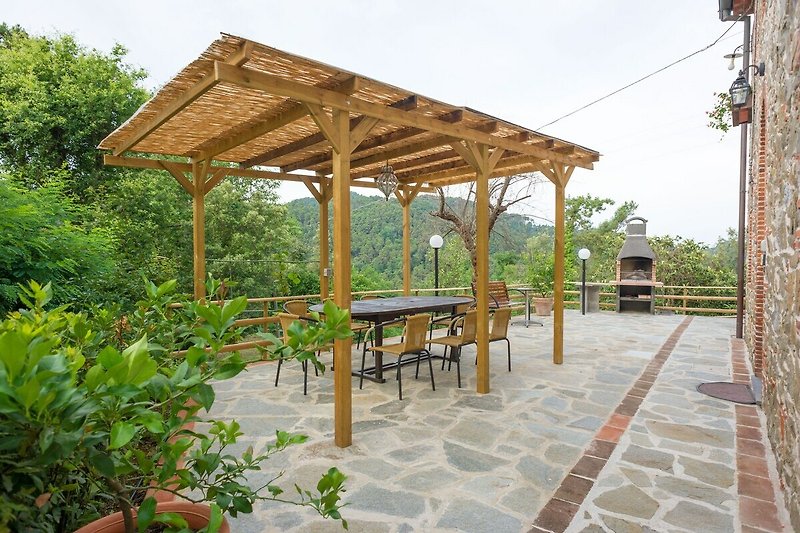Einladende Terrasse mit Pergola, Tisch und Stühlen unter schattigem Baum.