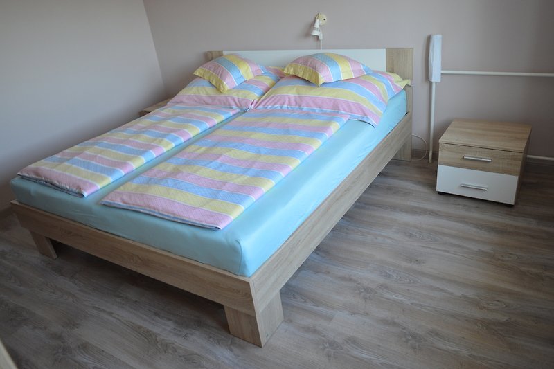 Gemütliches Schlafzimmer mit Holzbett, Matratze und Bettwäsche.
