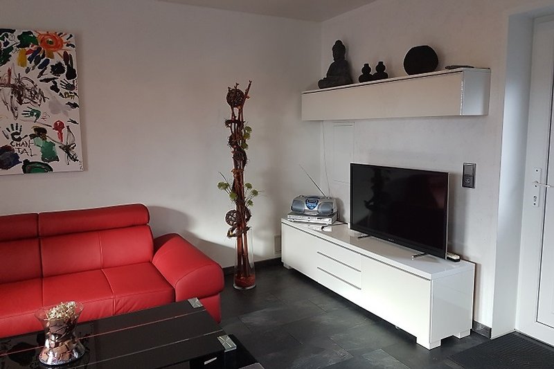 Wohnzimmer mit roter Ledercouch, Fernseher und Holzmöbeln.