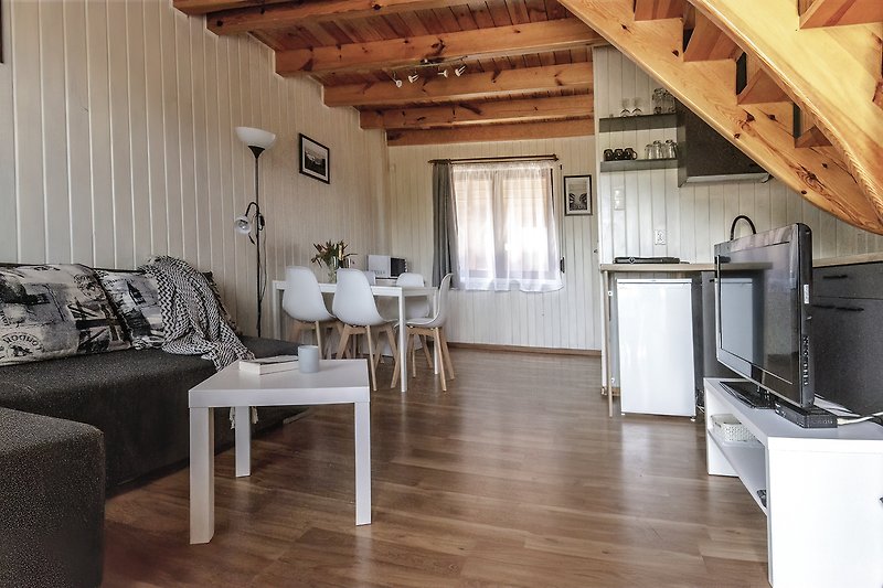 Moderne Küche mit Holzmöbeln, Beleuchtung und Küchengeräten. Gemütliches Wohnzimmer mit Couch und Tisch.