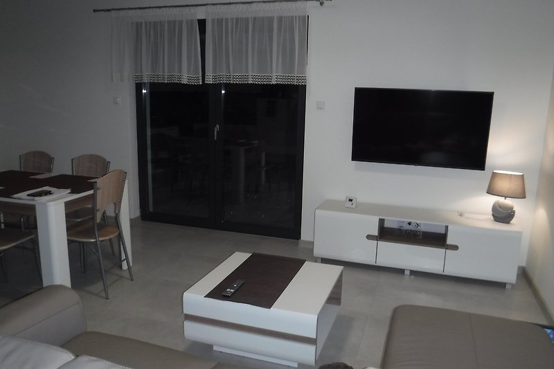 Modernes Wohnzimmer mit bequemer Couch, TV, Tisch und Stühlen.