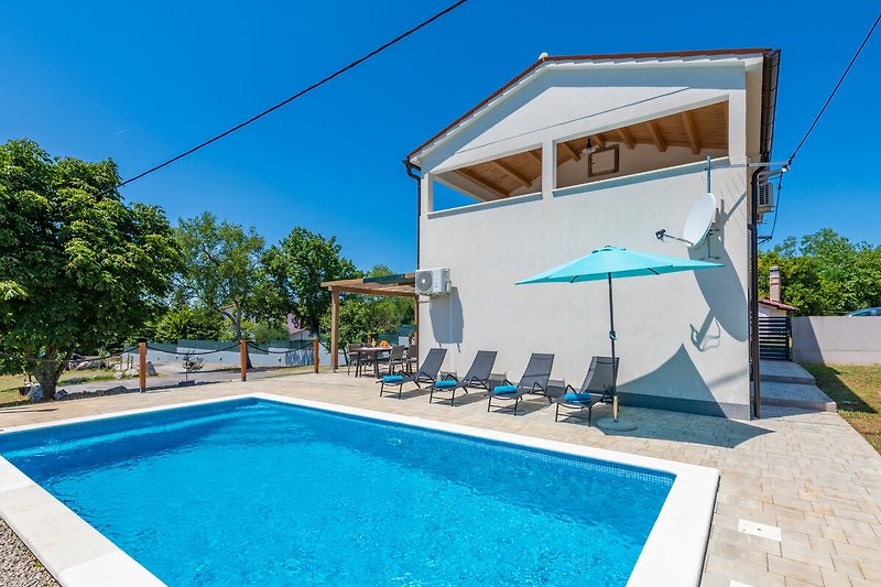 Schönes Ferienhaus mit Pool, Sonnenliegen und Blick auf das azurblaue Wasser.