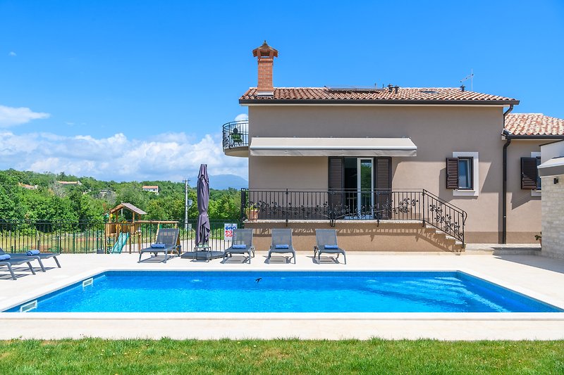 Schönes Haus mit Pool, umgeben von grünem Garten und blauem Himmel.