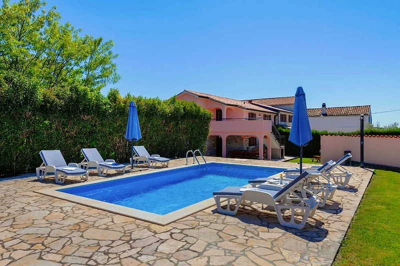 Pool mit Sonnenliegen, Sonnenschirm und bequemen Outdoor-Stühlen.