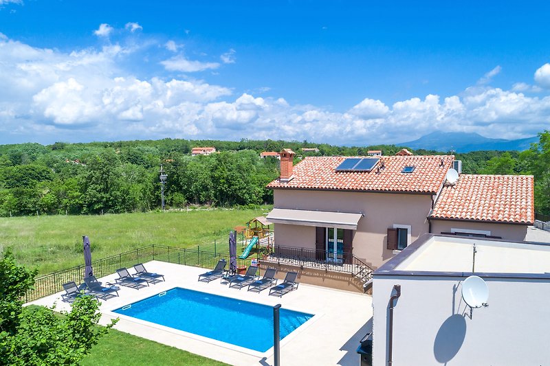 Schönes Haus mit Pool, umgeben von grünem Garten und blauem Himmel.
