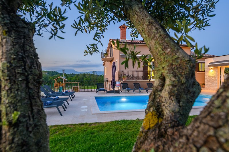 Schwimmbad mit Liegestühlen, umgeben von grüner Landschaft und einem schönen Haus.