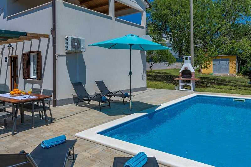 Schönes Ferienhaus mit Pool, Sonnenliegen und Blick auf das azurblaue Wasser.