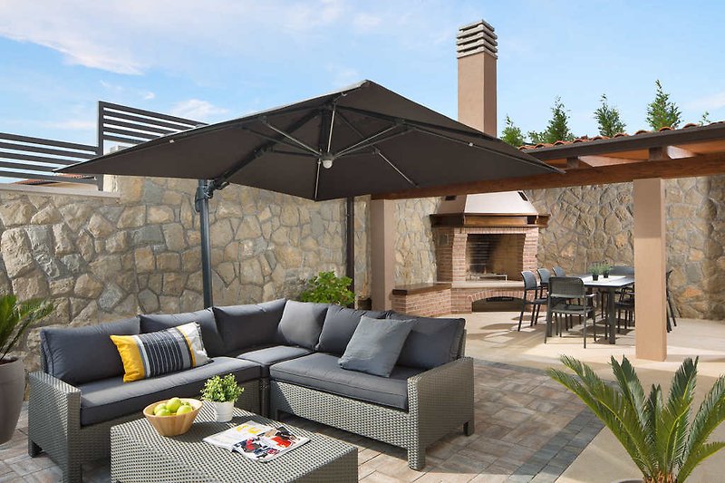 Bequeme Lounge-Terrasse, ein großer Esstisch und ein Holzkohlegrill