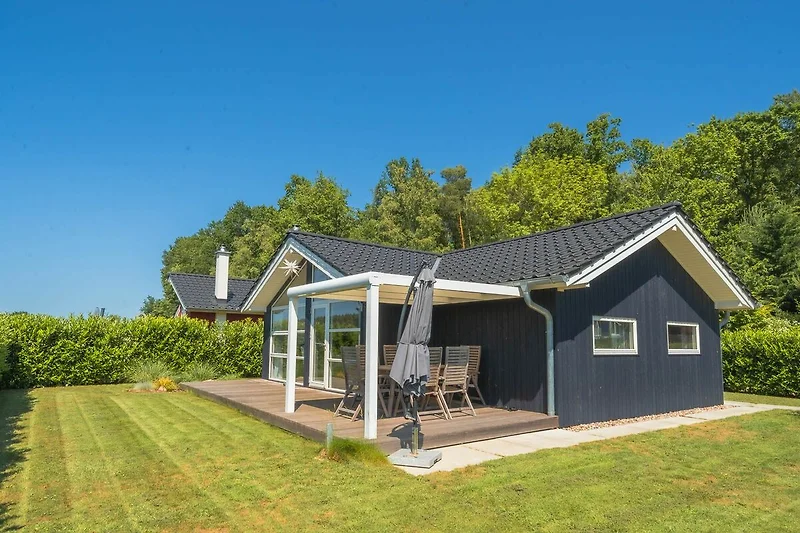 Haus mit Veranda und Gartenhäuschen im Schatten.