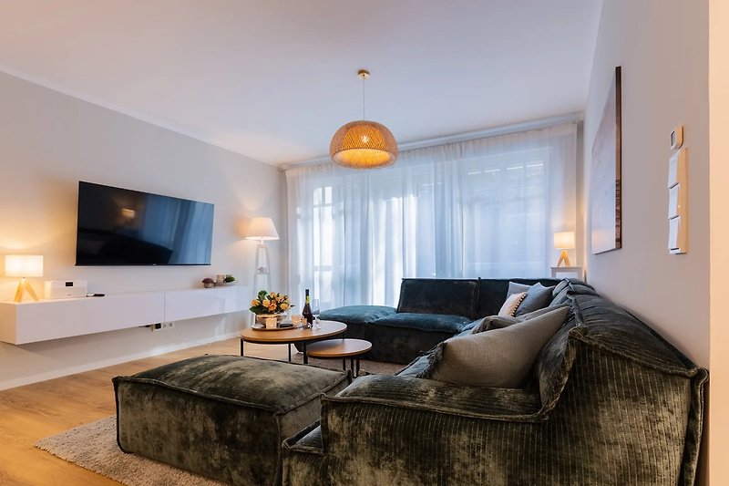Wohnzimmer mit bequemer Couch, Fernseher, Lampe & Bilderrahmen.