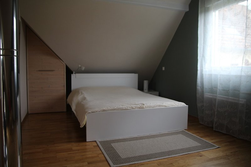 Schlafzimmer mit elegantem Bett und Vorhängen, Holz und Beton.