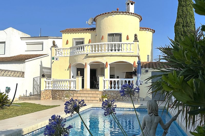 Villa mit Pool, Palmen und Balkon in tropischer Umgebung.