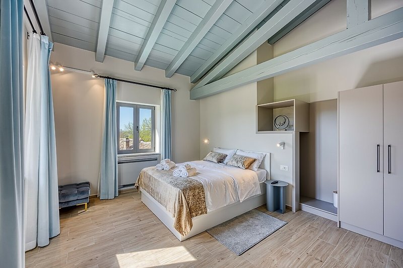 Schlafzimmer mit grauem Bett, Holzmöbeln und Fenster. Gemütliche Atmosphäre.