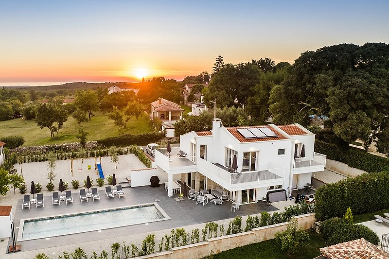 Sonnenuntergang über moderner Villa mit Garten und Stadtblick.