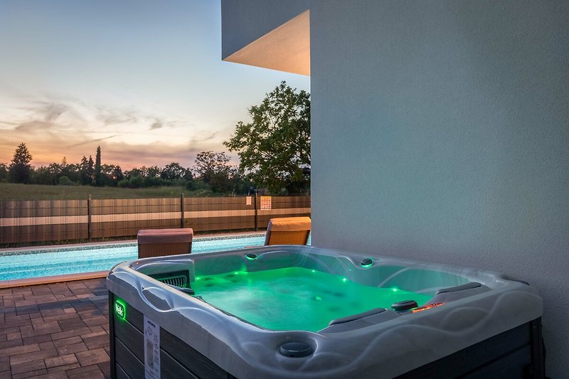 Relax in the jacuzzi surrounded by lush greenery and a clear blue sky.