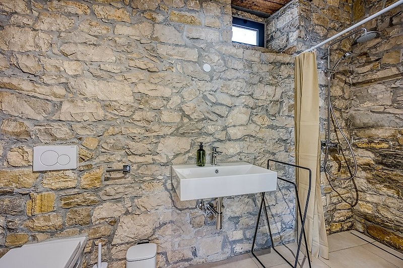 Modernes Badezimmer mit Steinwand, Holzdecke und Armatur.