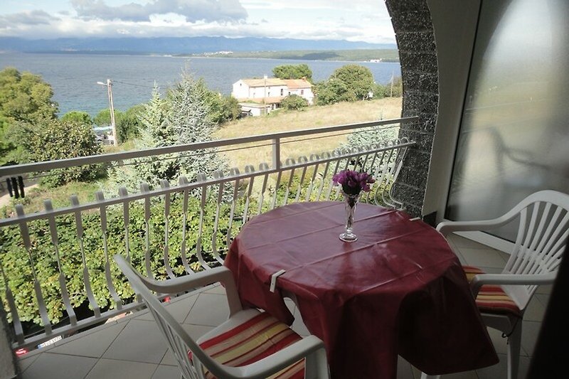 Balkon mit Tisch, Stühlen und Pflanzen. Schöner Ausblick auf Wasser und Himmel.
