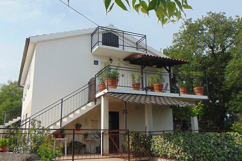 Ferienhaus mit Balkon, Pflanzen und Wolken.