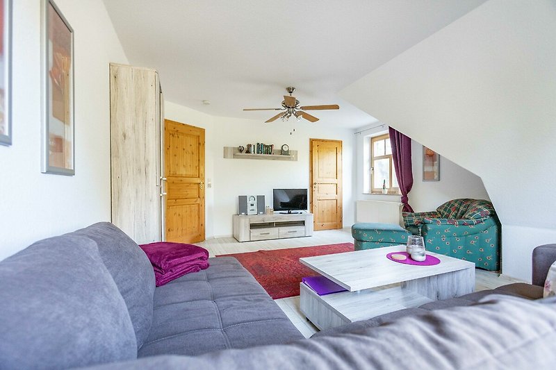 Gemütliches Wohnzimmer mit Holzmöbeln, lila Akzenten und bequemer Couch.